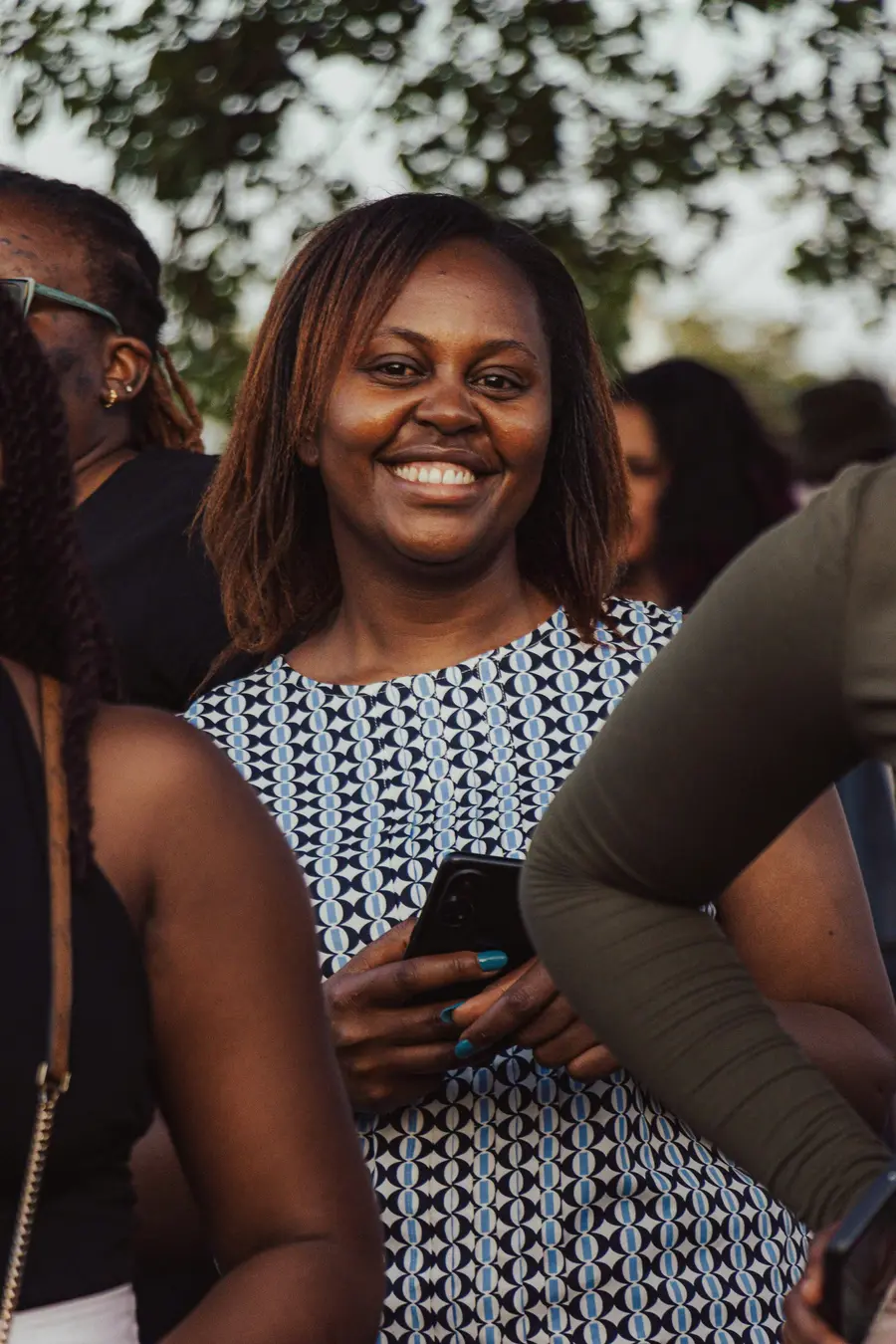 Mulher sorrindo com o celular na mão, ao ar livre