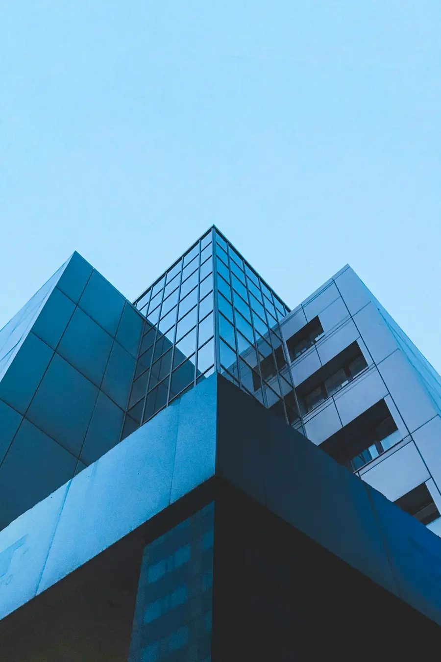 Prédio comercial moderno de vidro refletindo céu azul, visto de baixo