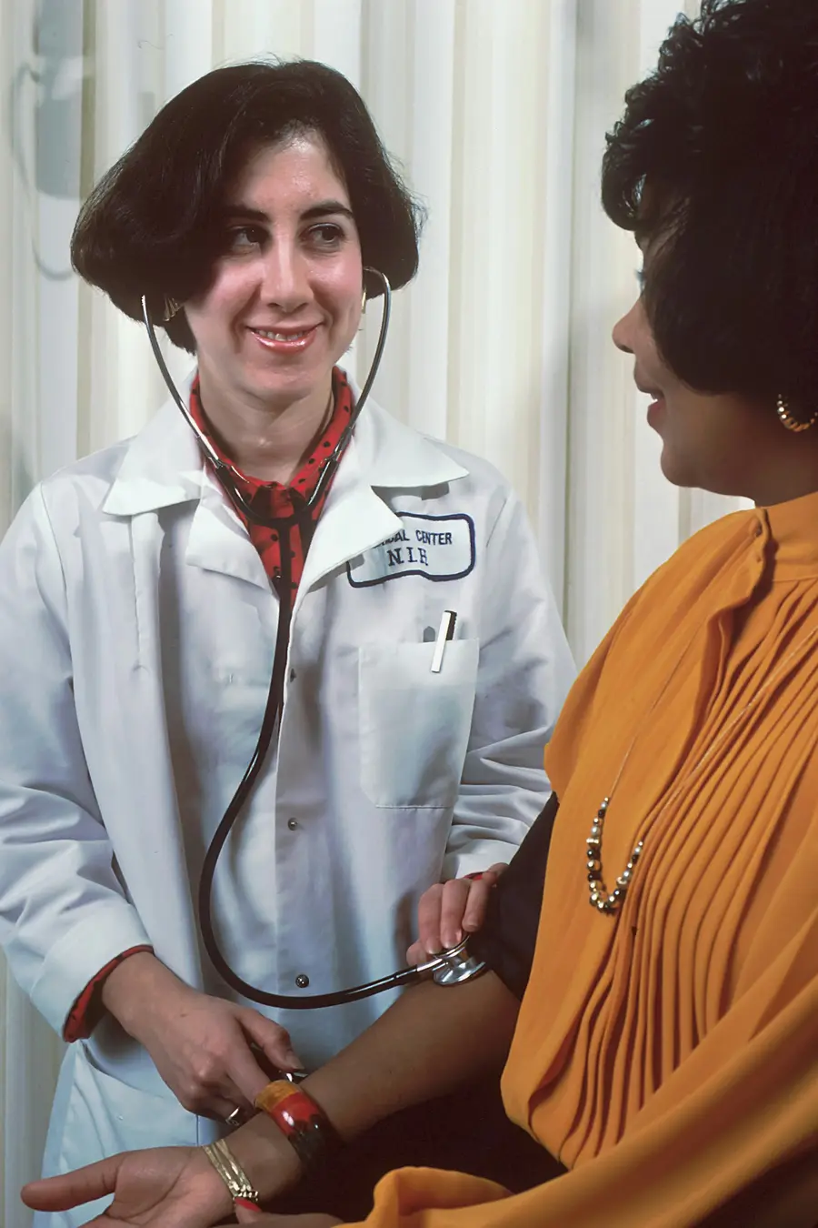 Médica de jaleco conversando com uma paciente