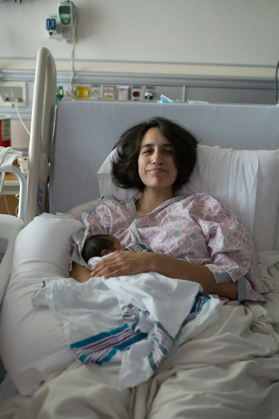 Paciente sorrindo com o bebê recém-nascido no leito da maternidade