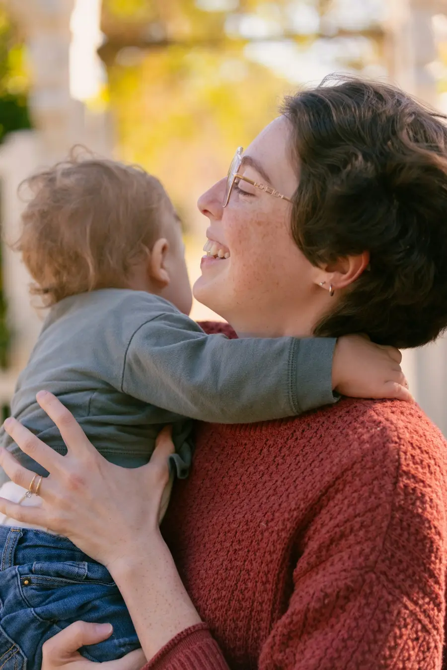 Mulher sorridente segurando o filho pequeno no colo e ensolarado