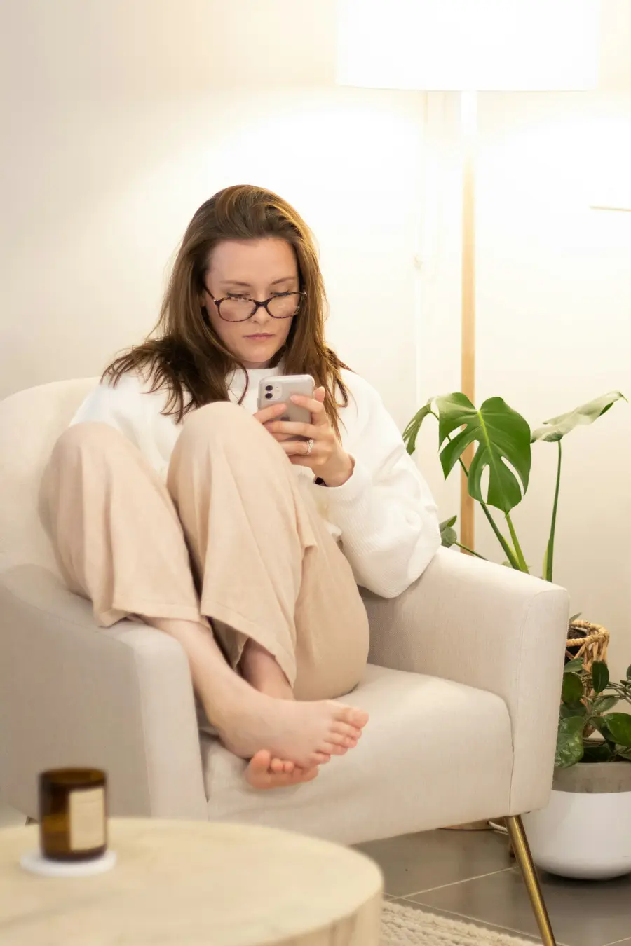 Mulher sorrindo ao conferir algo no celular, sentada numa poltrona