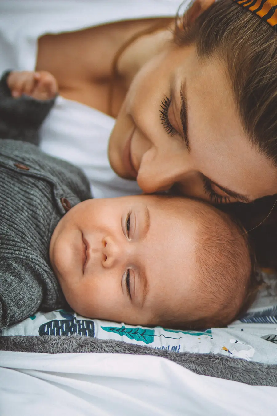 Mãe sorridente com o bebê no colo em quarto claro e tons suaves de azul