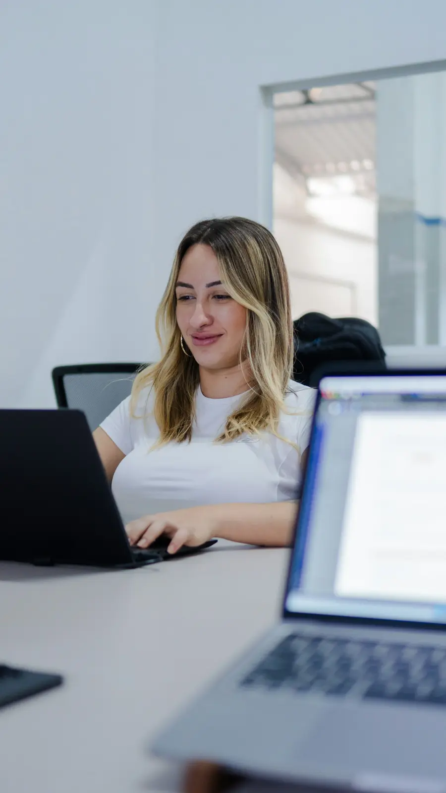 Mulher sorridente analisando gráficos no notebook em escritório claro, toques de azul
