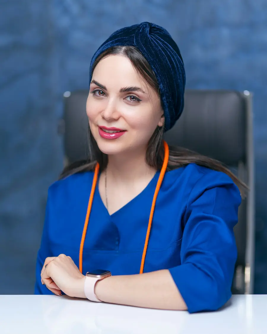 Médica elegante sorrindo de braços cruzados num corredor hospitalar claro e moderno