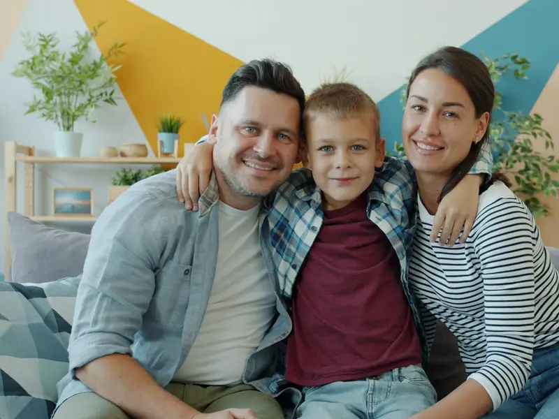 Pai, mãe e filho abraçados no sofá