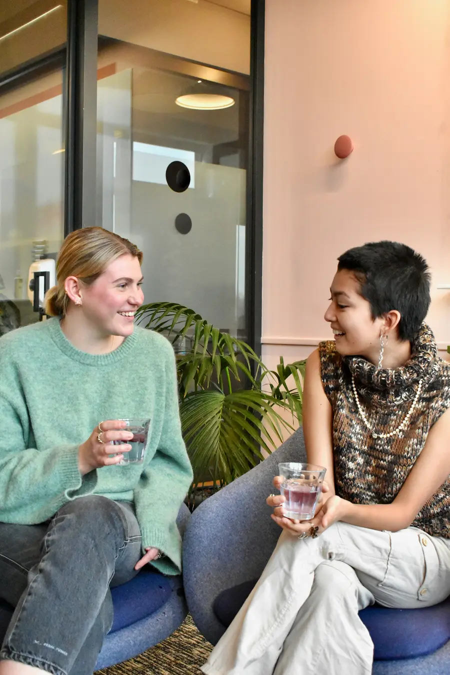 Funcionária sorridente conversando com a colega numa sala de reunião clara e detalhes em azul