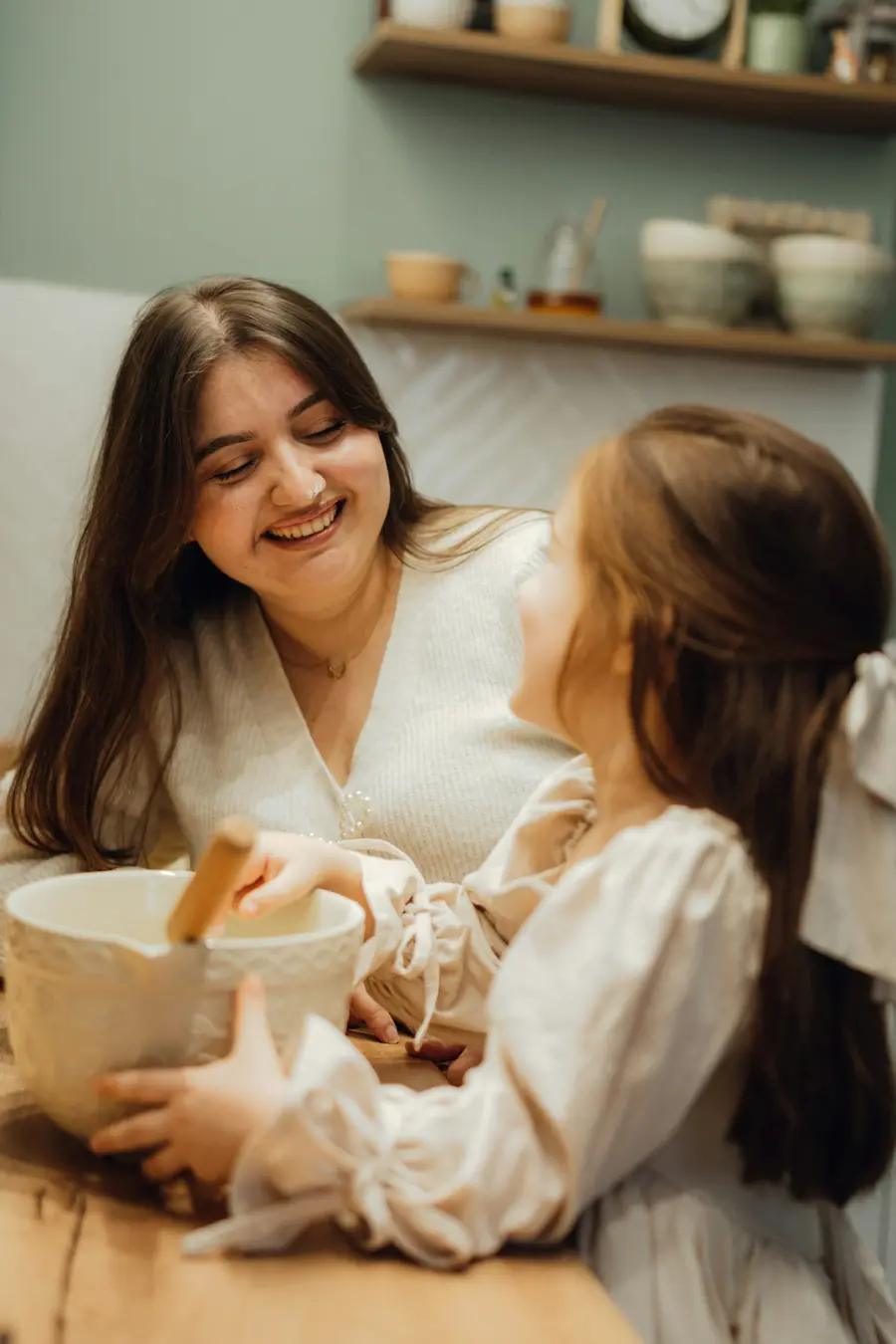 Senhora sorridente conversando com a filha adulta numa cozinha ou varanda clara, detalhes em azul