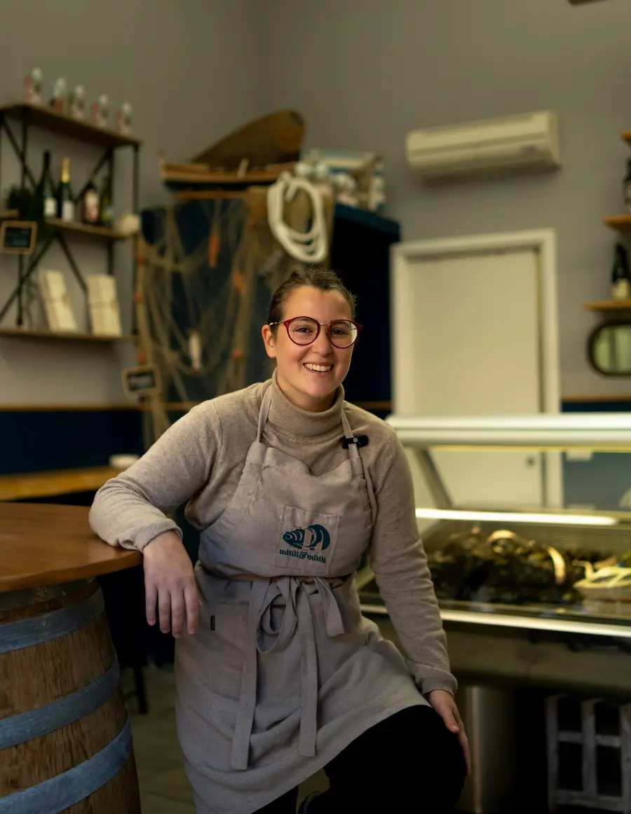 Dona de pequeno negócio sorridente atrás do balcão de uma loja ou café claro e detalhes em azul