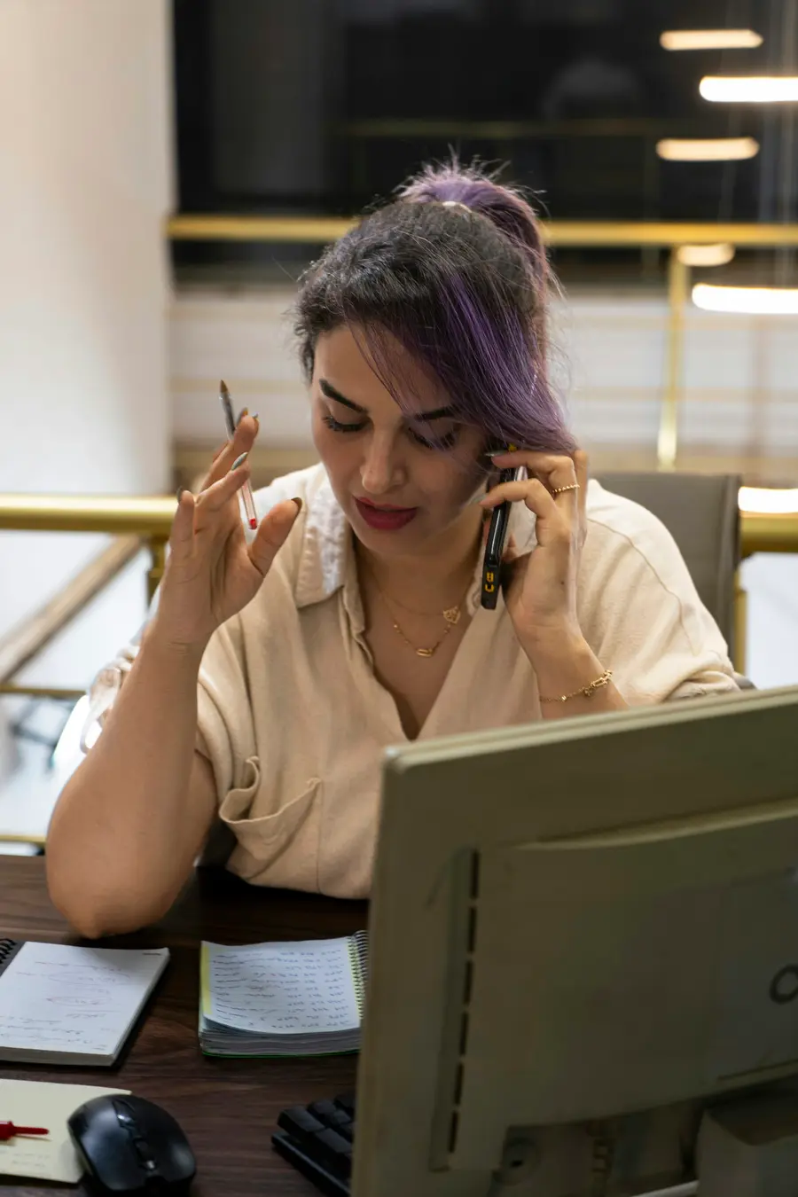 Mulher sorridente analisando papéis e o celular numa mesa clara perto da janela e detalhes em azul