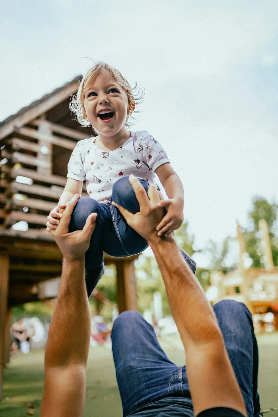 Família sorridente em parque com gramado e árvores, céu azul