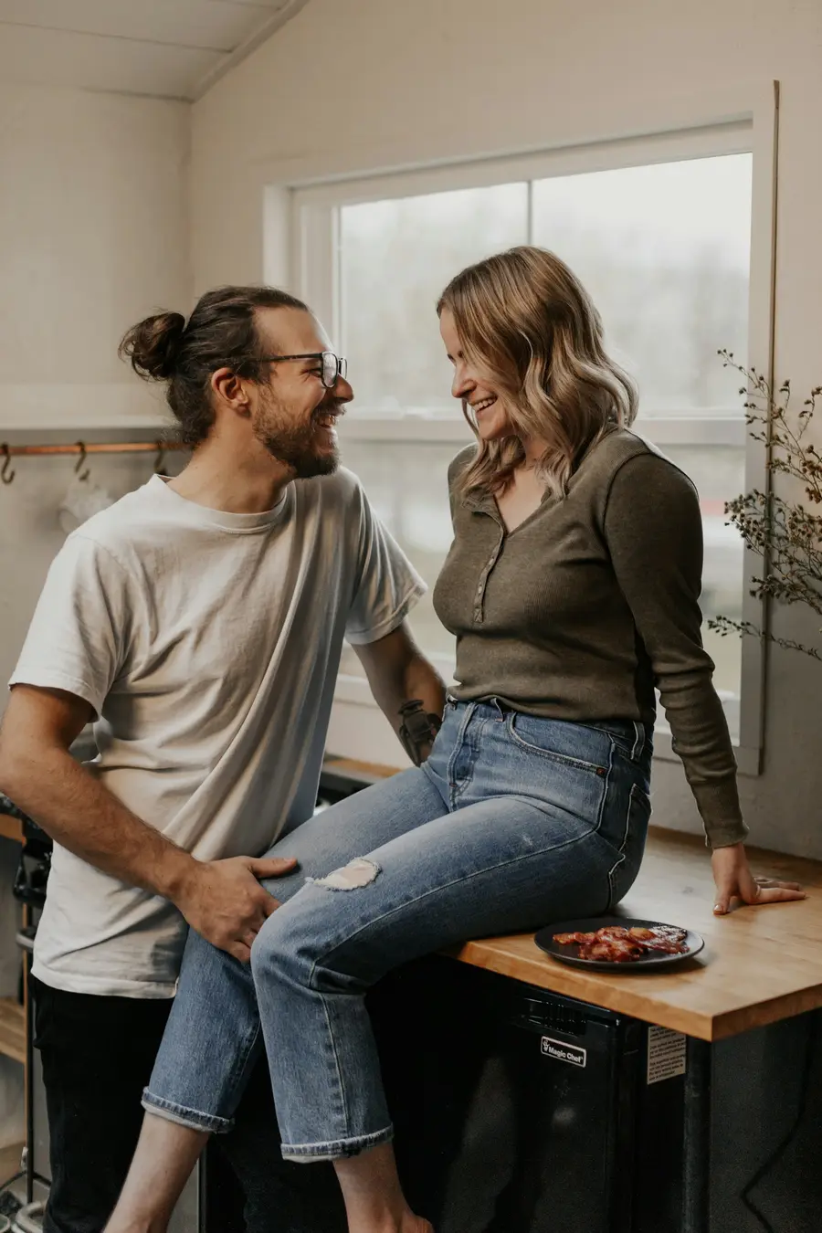 Casal jovem sorrindo e conversando na cozinha de casa clara