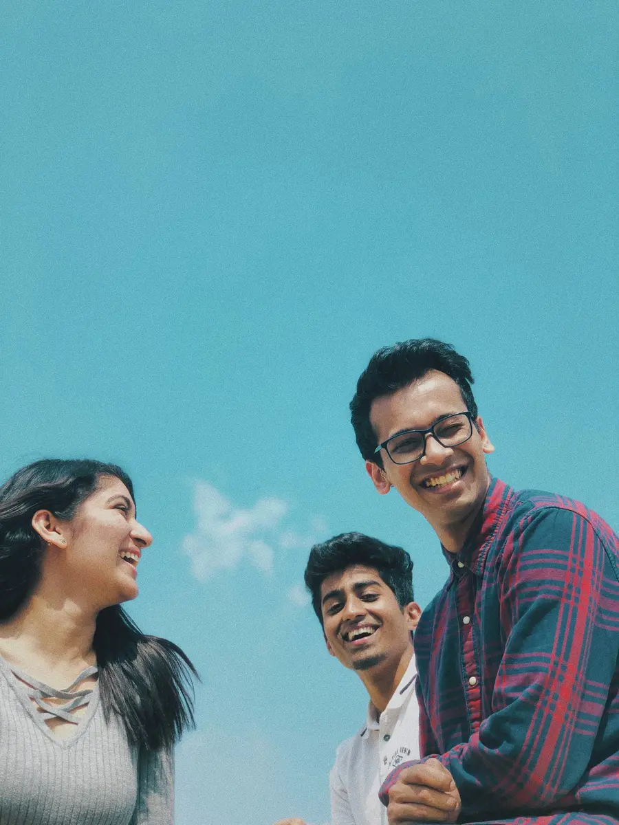 Três amigos sorrindo sob céu azul