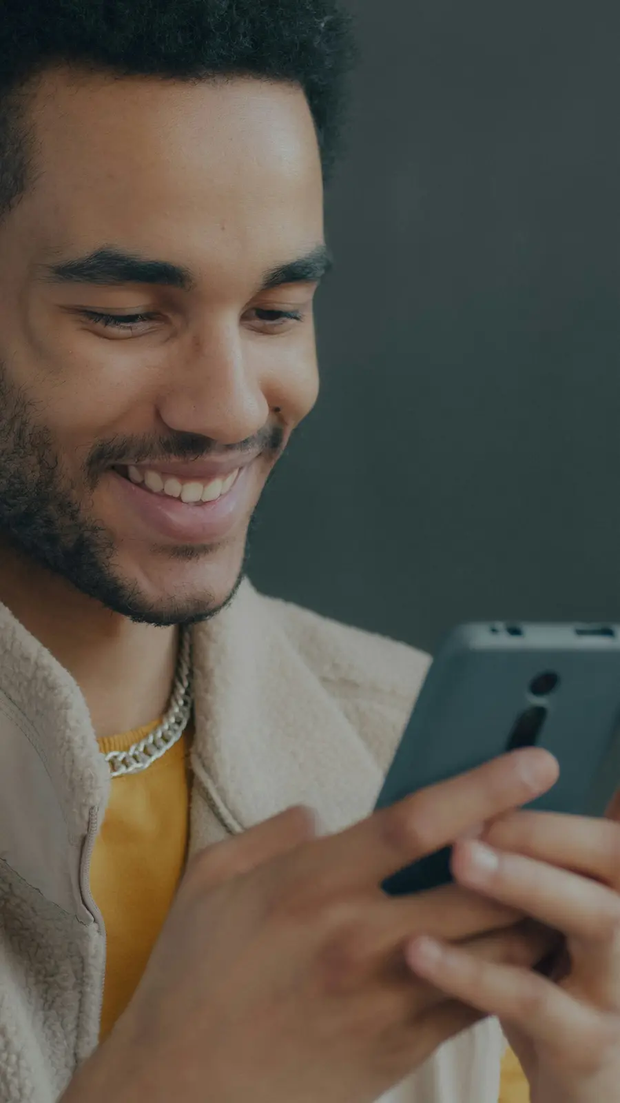Homem de uns 35 anos sorrindo enquanto digita no celular em casa clara, detalhes em azul