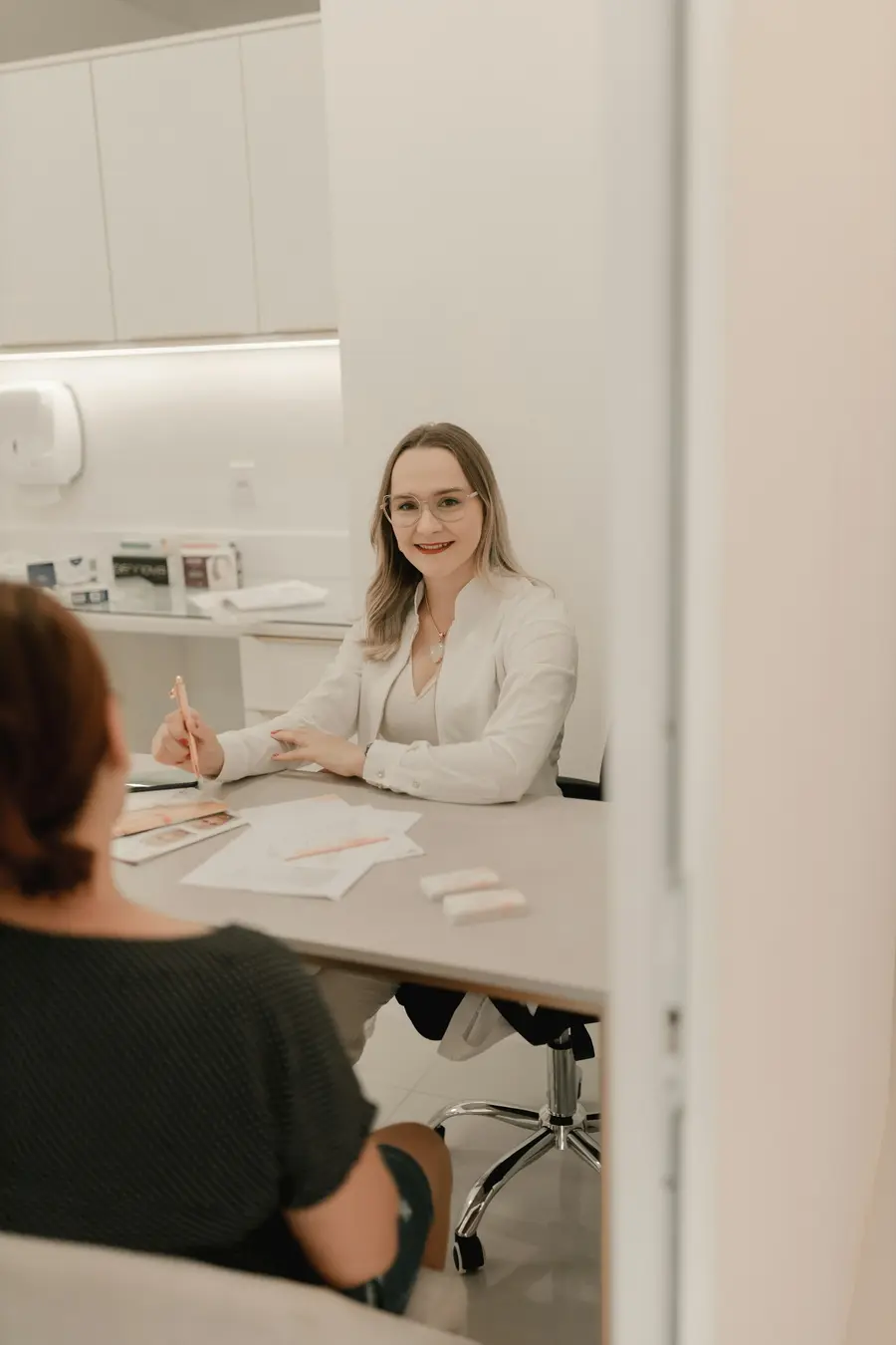 Médica sorridente atendendo um paciente adulto em consultório claro, tons de branco e azul