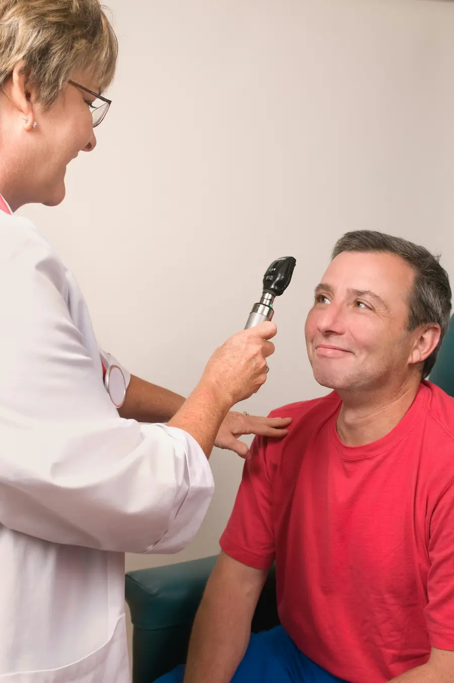 Médico geriatra sorrindo ao lado de um paciente idoso num consultório claro, com detalhes em azul