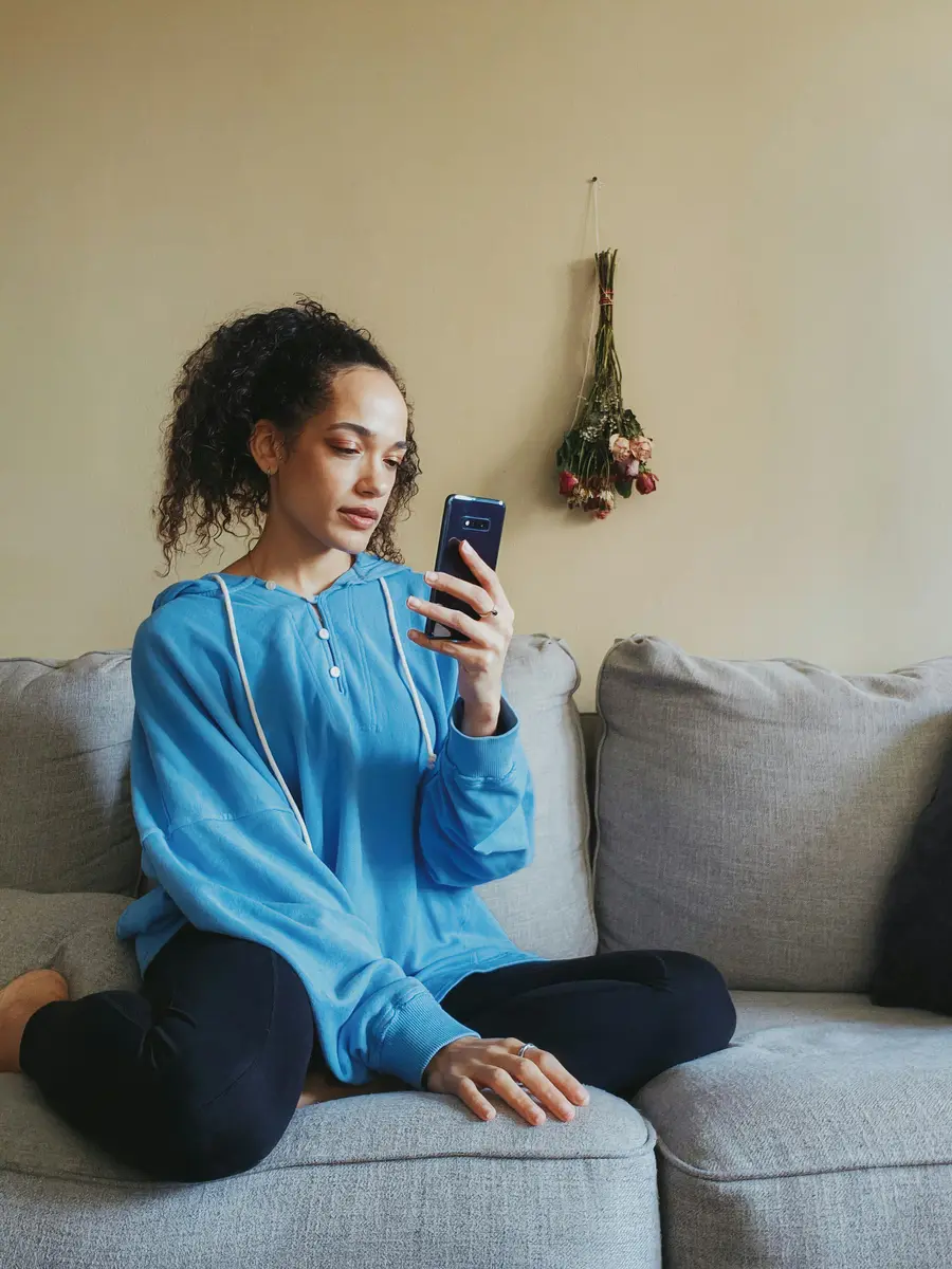 Mulher de blusa azul sentada no sofá olhando o celular