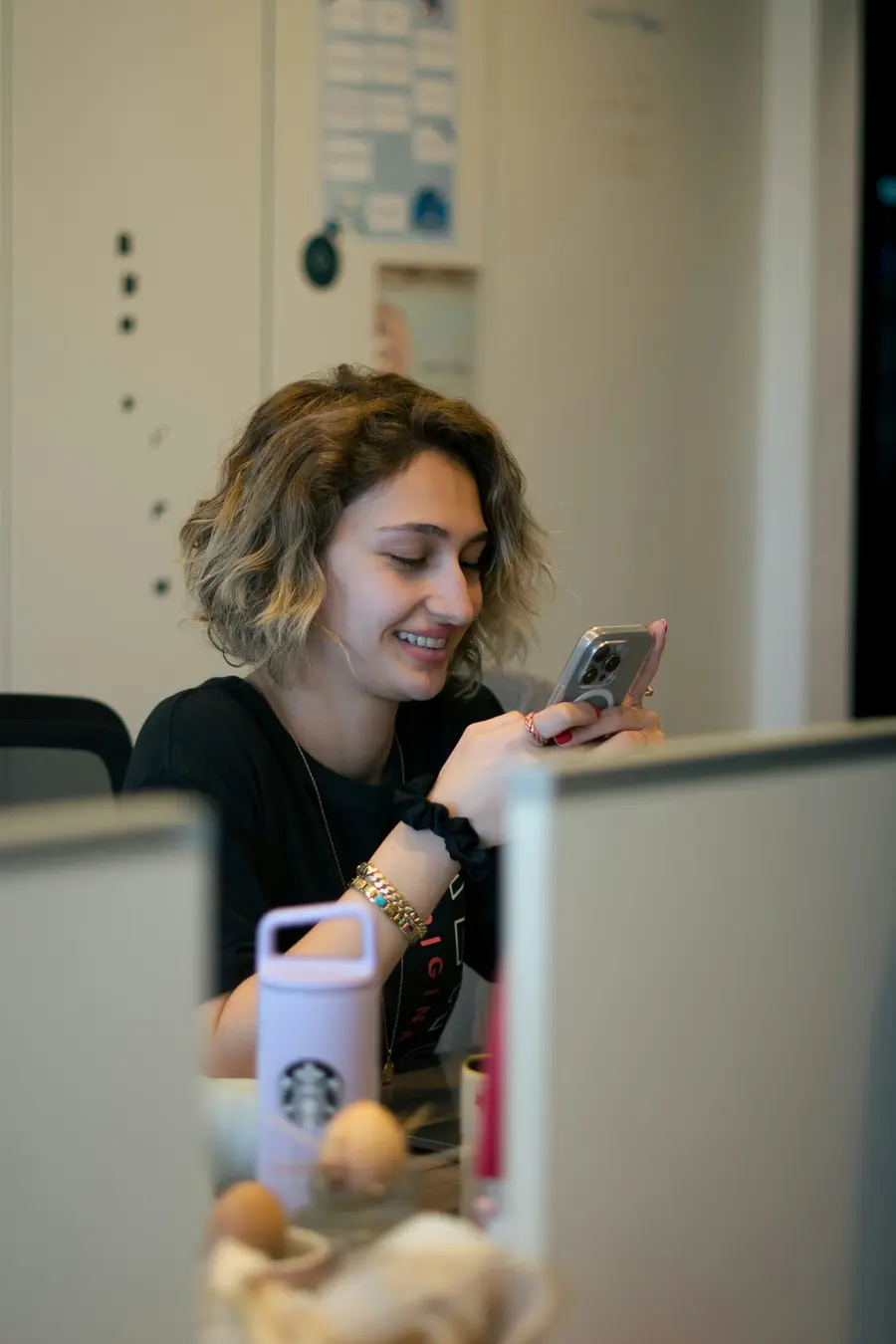 Mulher sorridente ao telefone, sentada à mesa com documentos e notebook num escritório claro