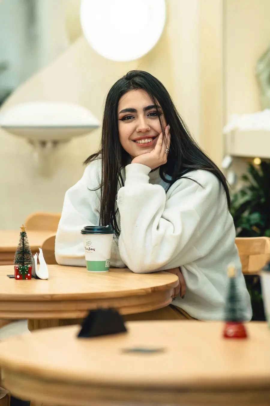Mulher jovem sorridente sentada num café claro olhando o celular