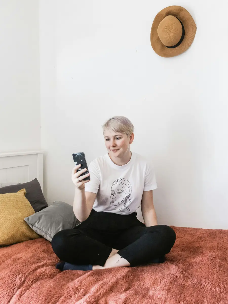 Mulher sorrindo ao usar o celular, sentada na cama