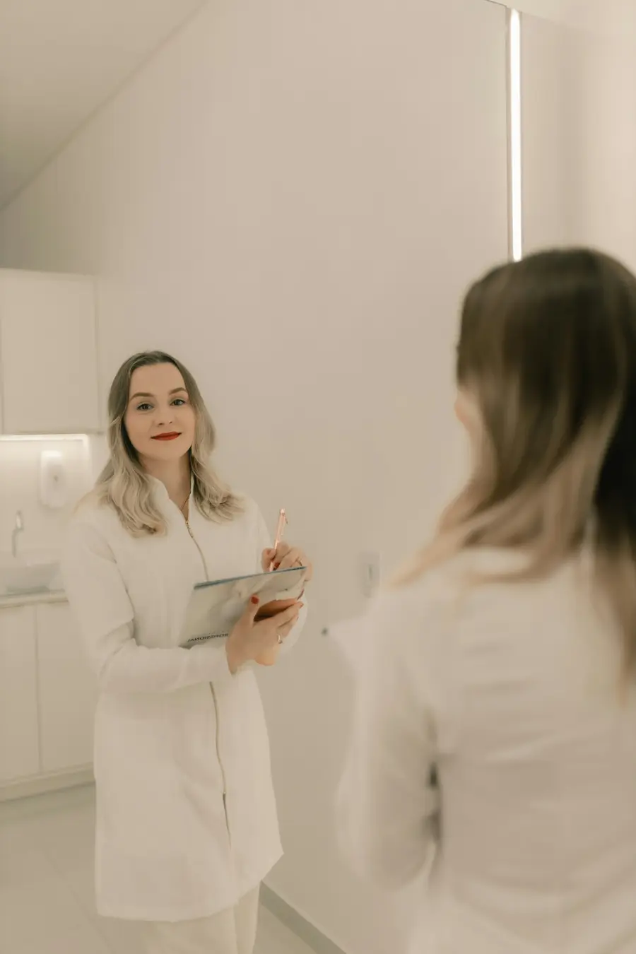 Médico jovem sorrindo enquanto conversa com um paciente num consultório moderno e claro, com detalhes em azul