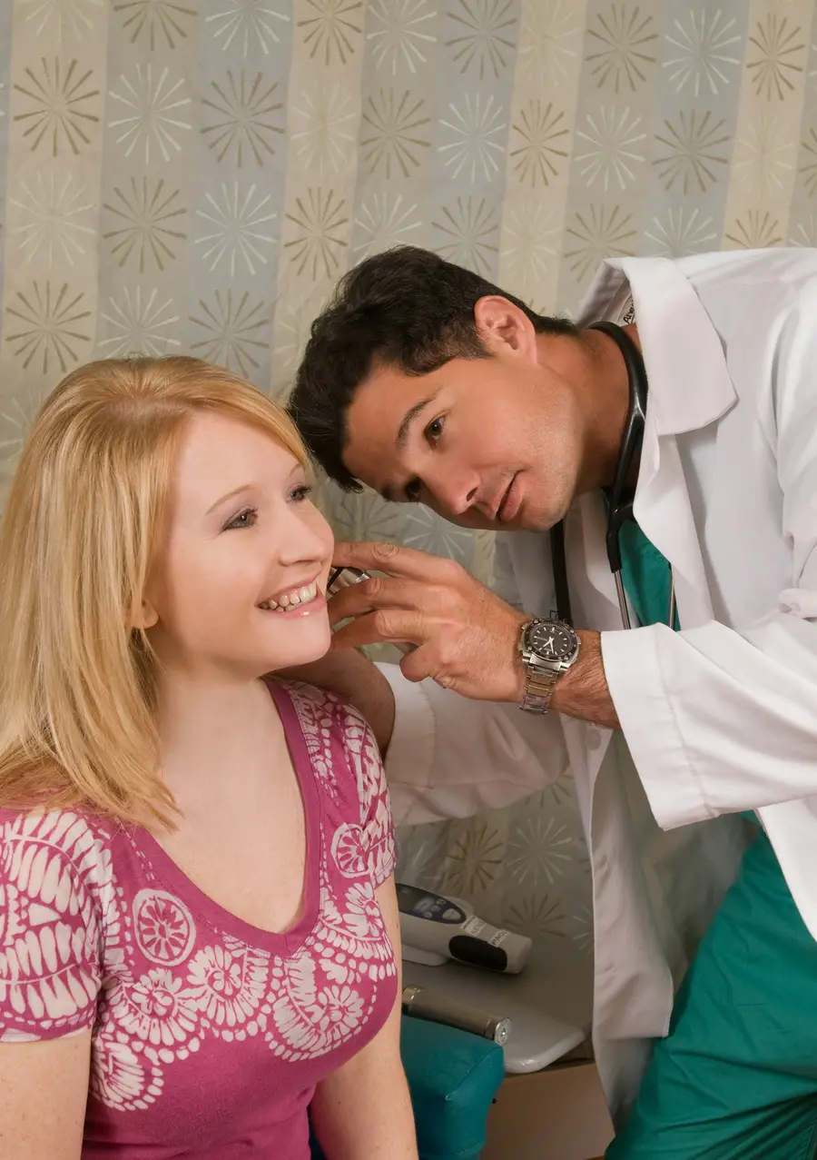 Médico jovem sorrindo enquanto conversa com um paciente num consultório moderno e claro, com detalhes em azul
