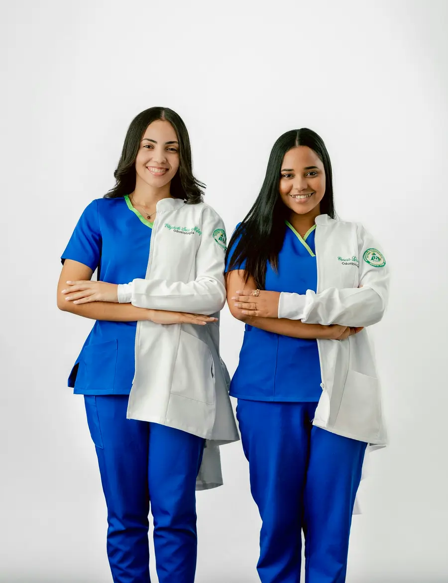 Duas profissionais de saúde de uniforme azul e jaleco branco