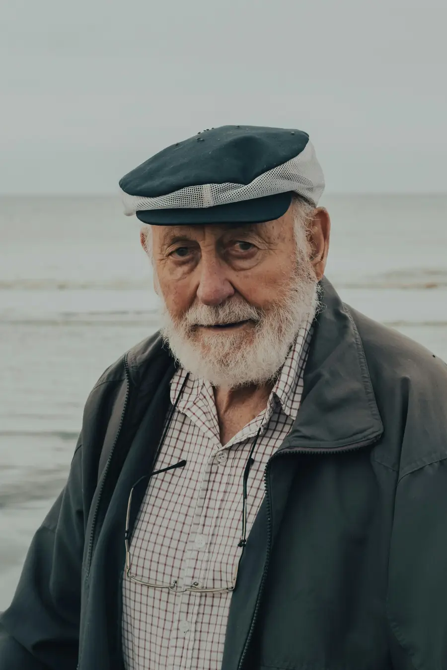 Homem de cerca de 60 anos sorrindo ao ar livre perto do mar, céu azul, roupa clara