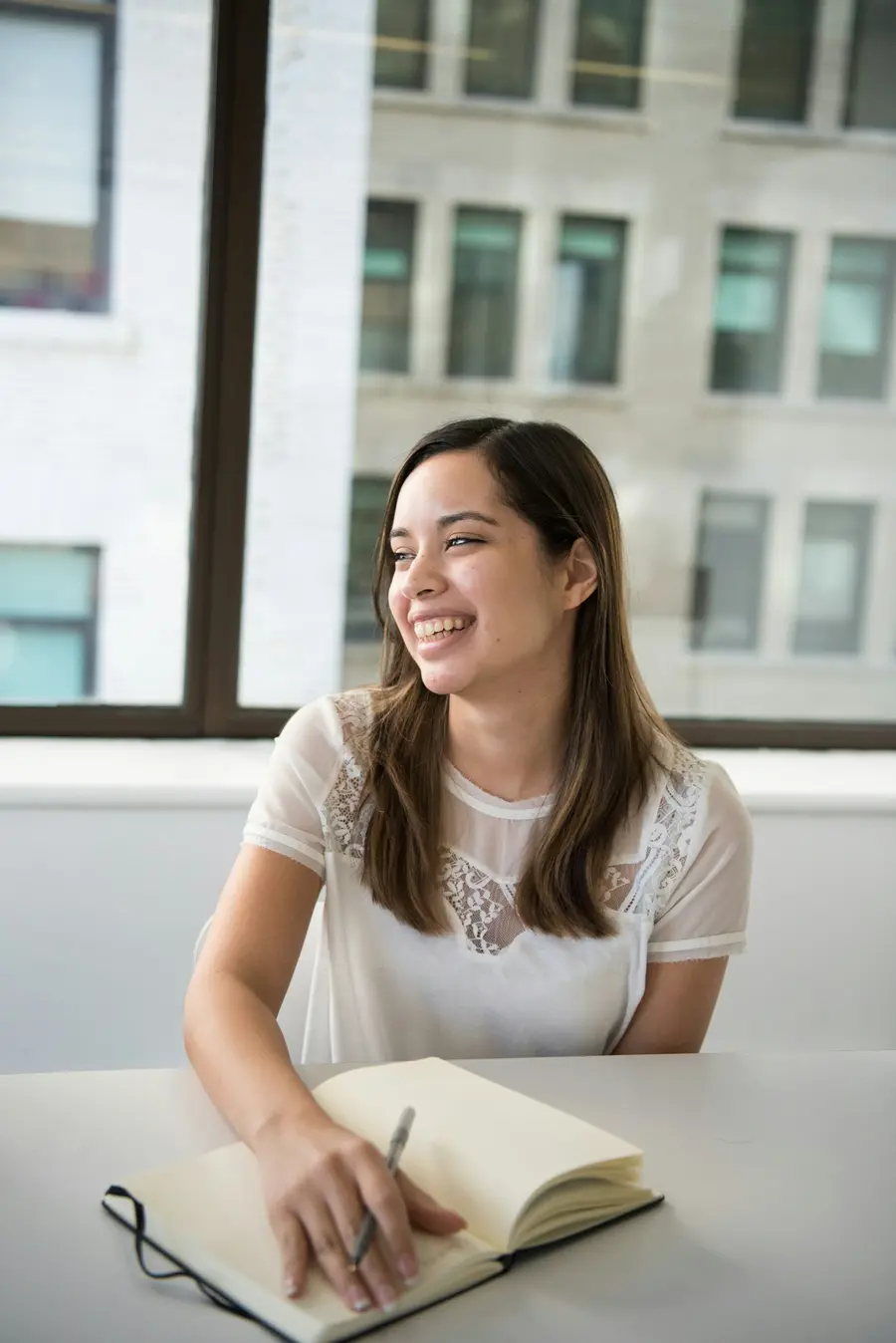 Mulher sorrindo com um livro aberto na mesa