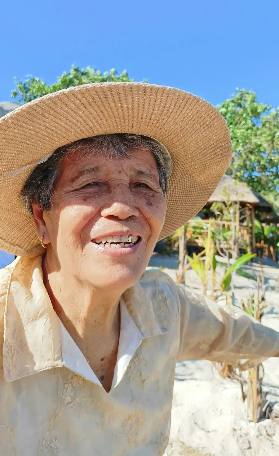 Senhora de cerca de 60 anos sorrindo num parque arborizado e claro de São Paulo, com céu azul