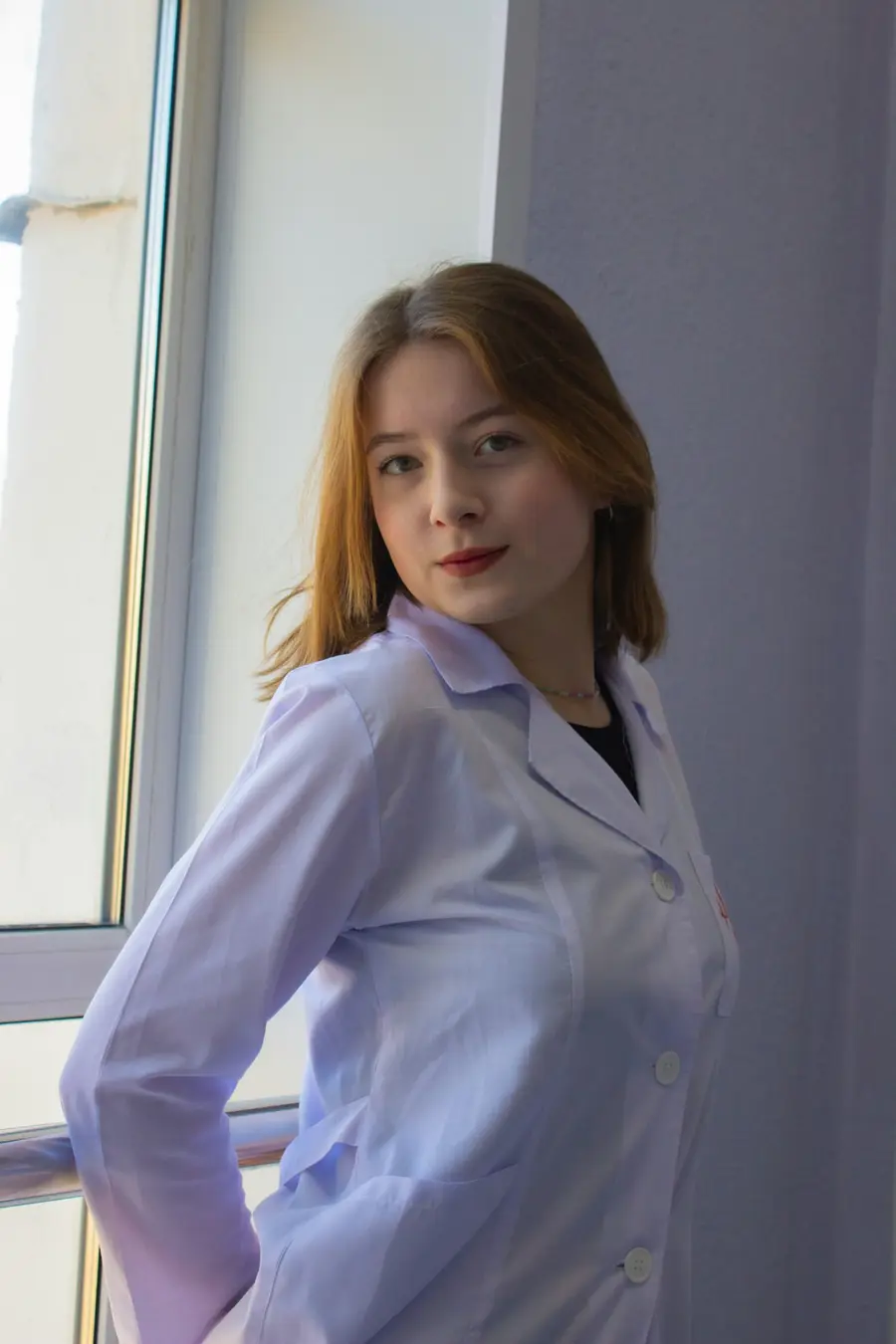 Médica sorridente de jaleco branco num consultório claro com plantas e, detalhes em azul