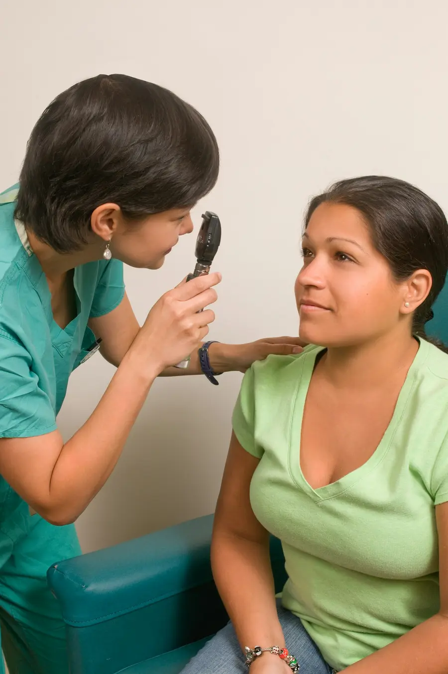 Pediatra sorridente examinando criança com a mãe, consultório claro